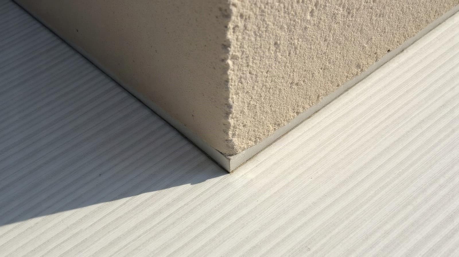 Vue rapprochée d'un angle de terrasse en béton ciré terminé, ombre portée nette sur la matière