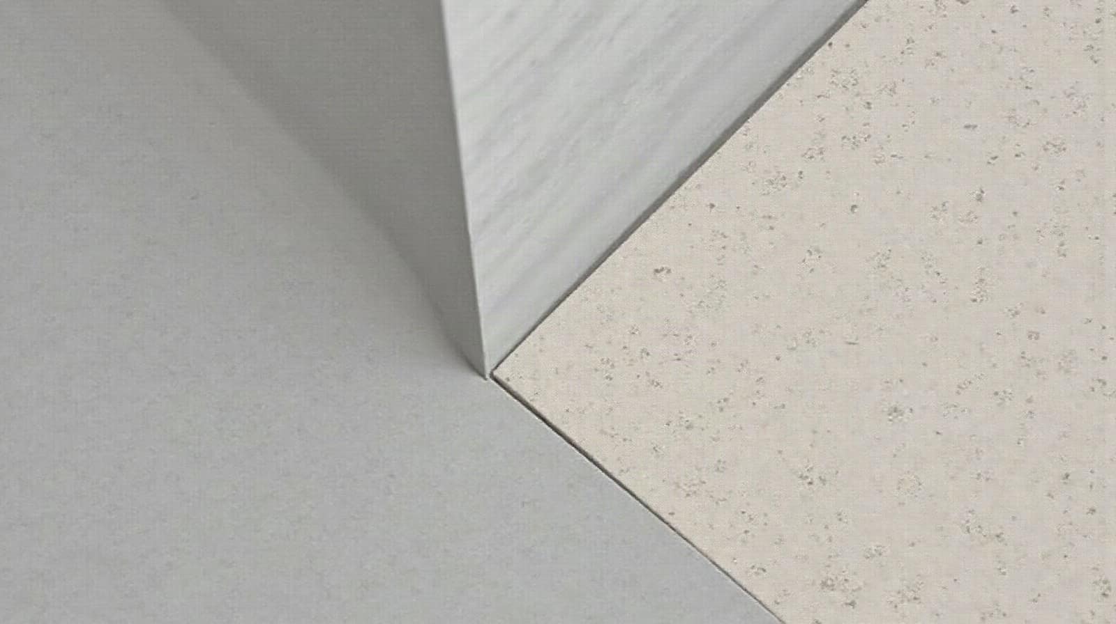Détail d'une jonction entre un sol en béton ciré fini et une plinthe fraîchement posée, matériaux distincts visibles