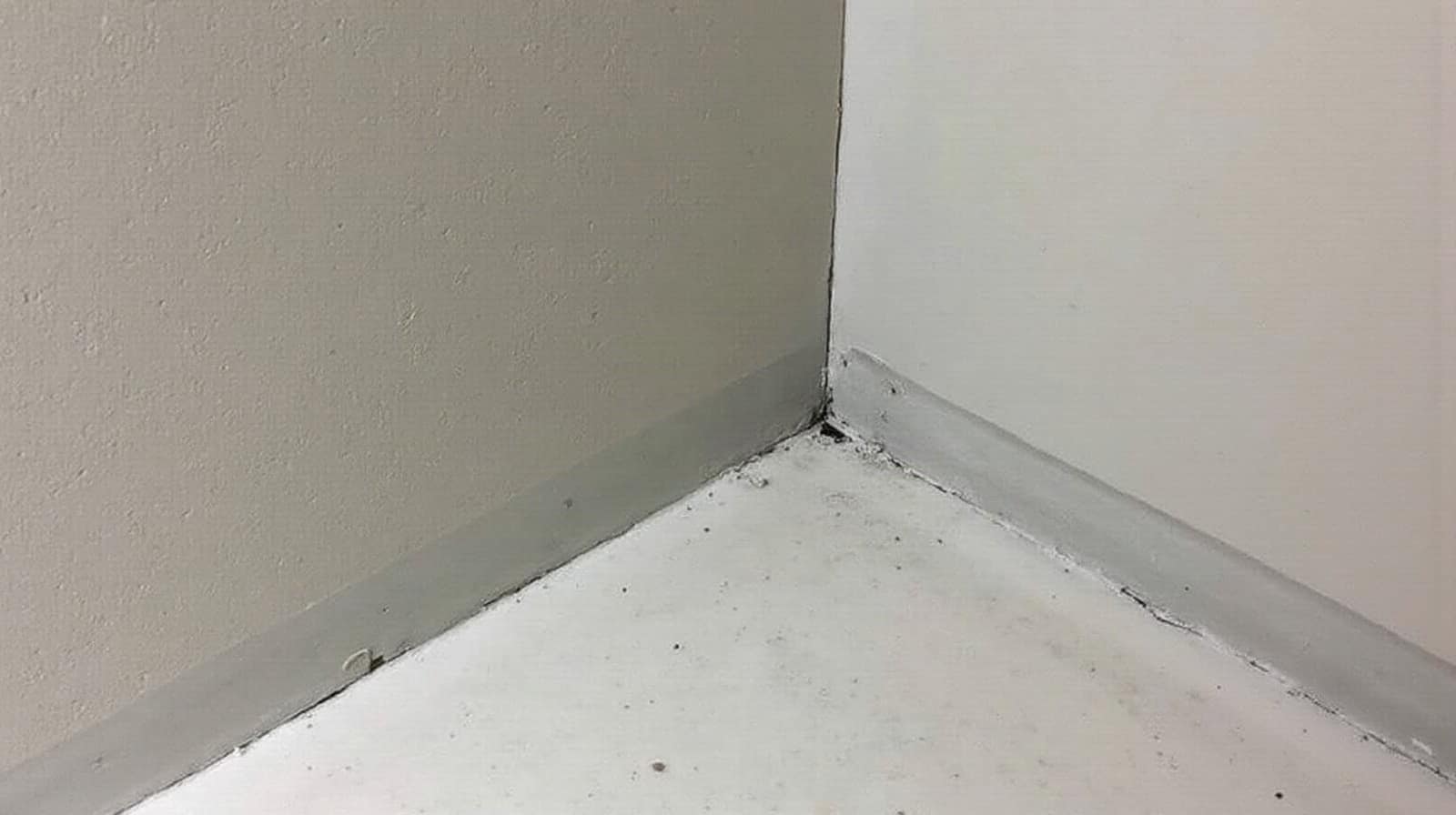 Sol fini en béton ciré uniforme dans une pièce d'appartement ancien, angle de mur d'origine en arrière-plan discret