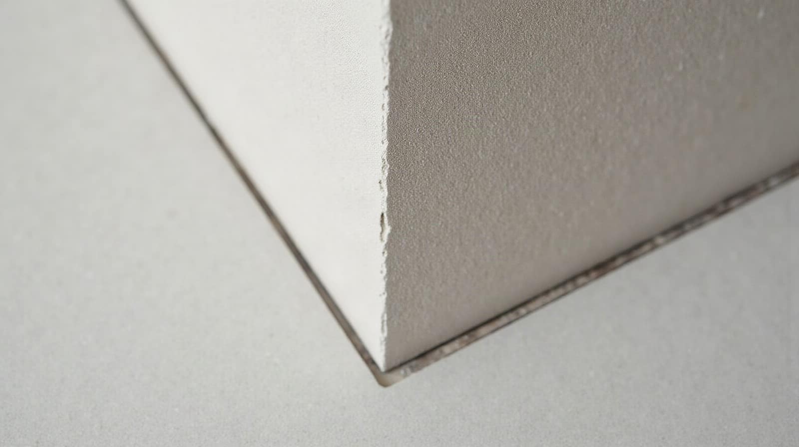 Vue rapprochée d'un angle de mur et de sol en béton ciré fini, teinte homogène sur les deux surfaces